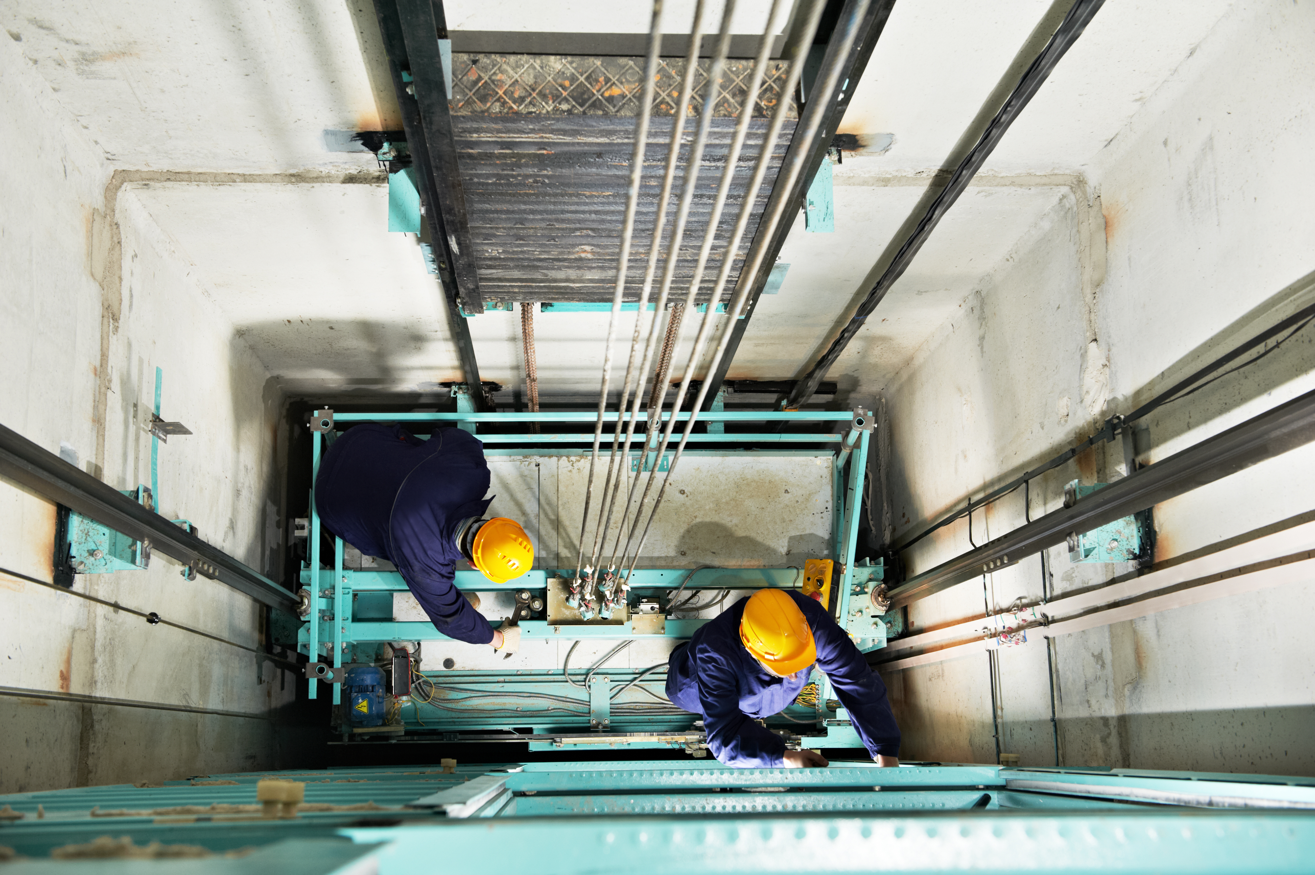 two male technician machinist worker at work adjusting elevator mechanism of lift with spanner