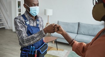 Waist up portrait of African-American handyman wearing mask bumping fists with client as con tactless greeting, copy space