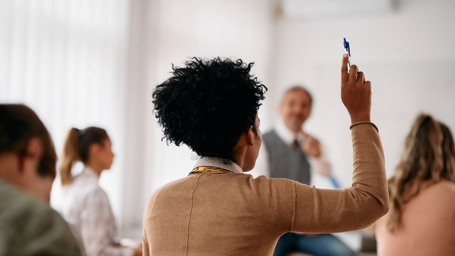 Back view of African American student raising her arm to answer a question during lecture in the classroom.