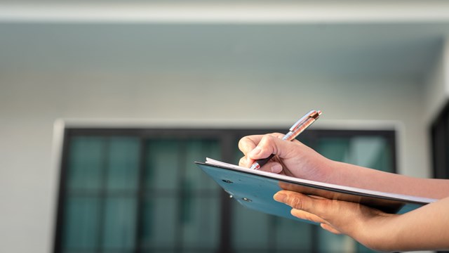 Action of an engineer is writing down on the clipboard paper to verify the quality of new house that already finish (as blurred background). Home developer business and industrial photo.
