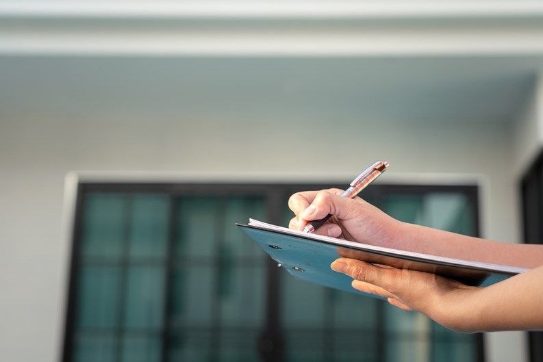 Action of an engineer is writing down on the clipboard paper to verify the quality of new house that already finish (as blurred background). Home developer business and industrial photo.