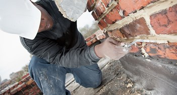 Masonry Maintenance Construction mason uses trowel to add mortar to brick joint.
